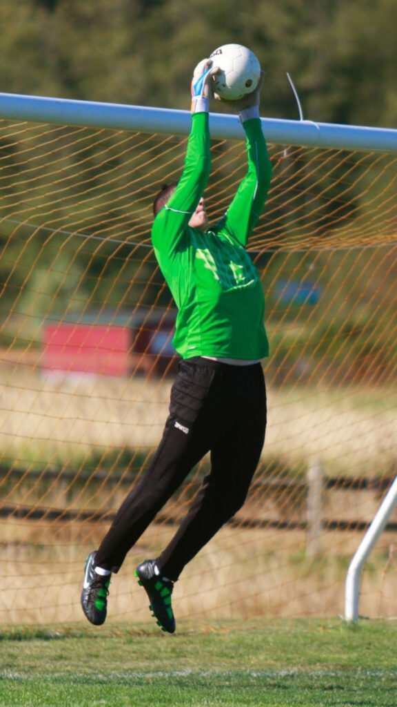 A tall soccer goalkeeper jumps to save a ball during private soccer goalkeeper training lessons